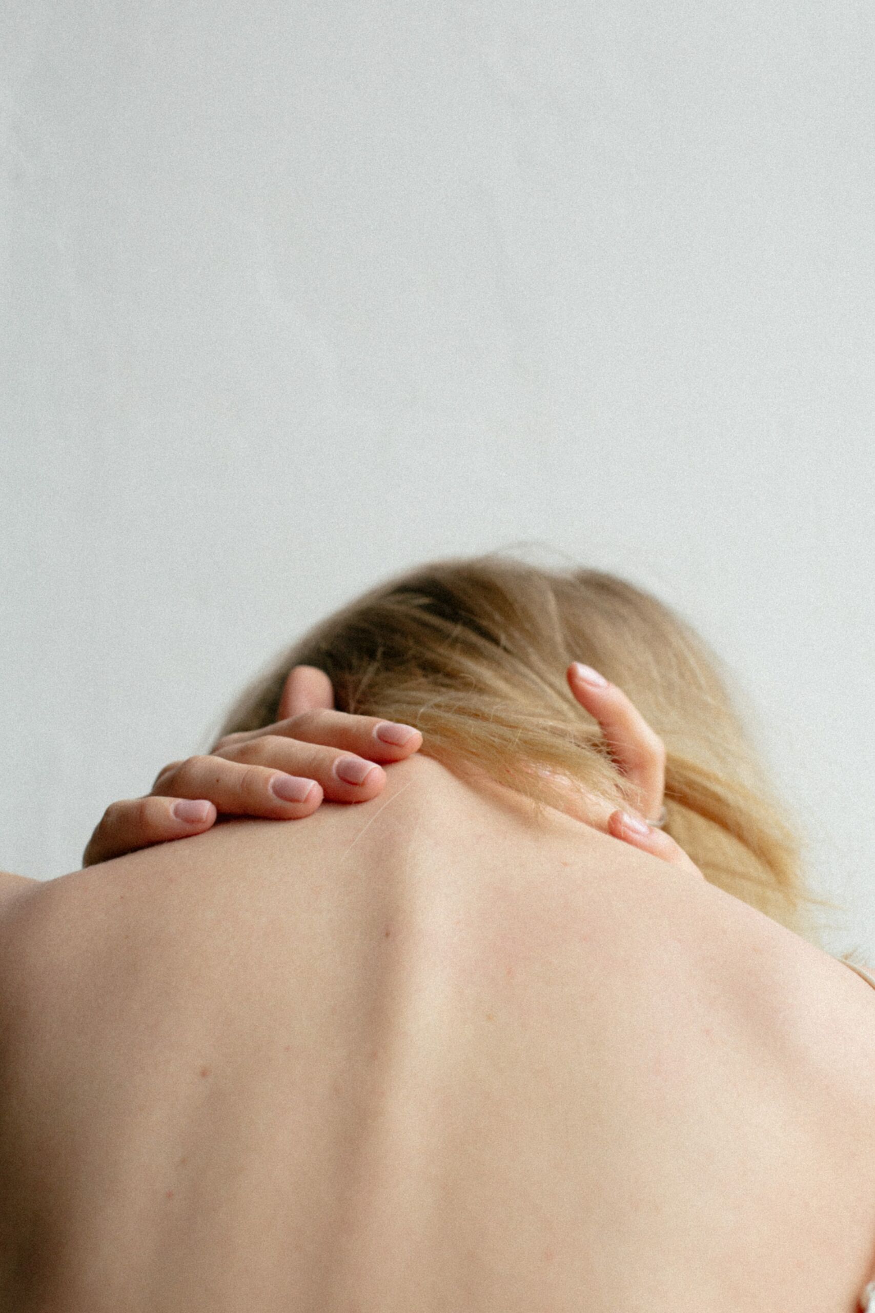 chronische Schmerzen behandeln - ein Schmerzgedächtnis bildet sich häufig bei längerfristigen Schmerzen - Frau mit Nackenschmerz, die ihre Nackenmuskeln berührt
